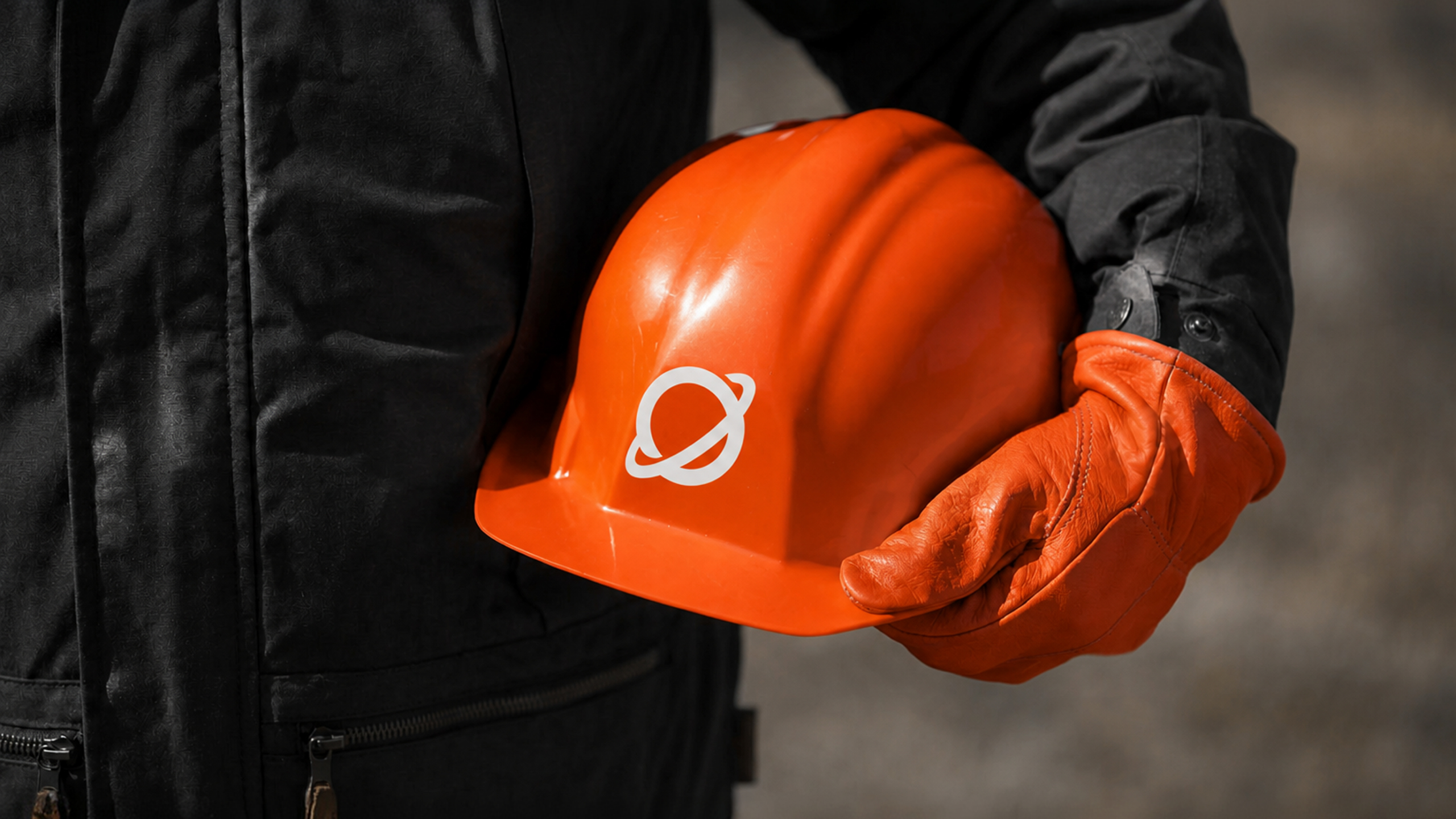 A worker in orange gloves holding a Saturn-branded safety helmet